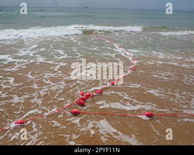 Buoys on a rope in sea water. The lifebuoys are pink restraints to alert people to the depth of the water. Rescue of the drowning. Delimiting a place on sandy beach between hotels. Wave with bubbles Stock Photo