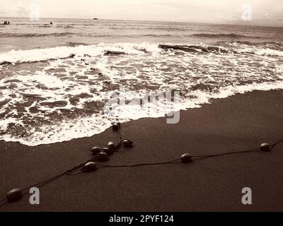 Buoys on a rope near sea water. The buoys are bright pink restraints to alert people to the depth of the water. Sepia. Delimiting a place on a sandy beach between hotels. Waves with bubbles Stock Photo