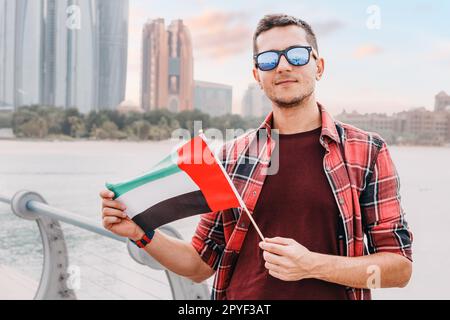 Young man freelancer or student with UAE flag against scenic skyscrapers in Abu Dhabi. Immigration, education and arab emirates citizenship concept Stock Photo