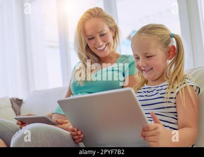 Doing some research on becoming a big sis. a pregnant woman and her little daughter using digital tablets at home. Stock Photo