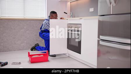 Repairman In Overalls Repairing Cabinet Hinge Stock Photo