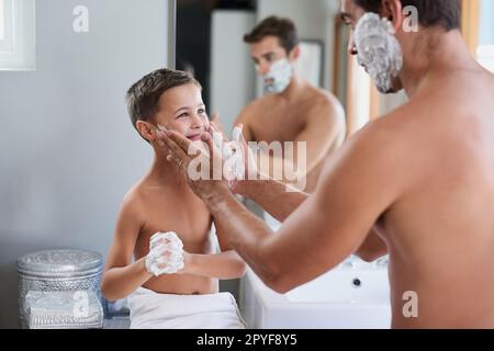 This is how you do it. a handsome young man teaching his son how to shave in the bathroom. Stock Photo