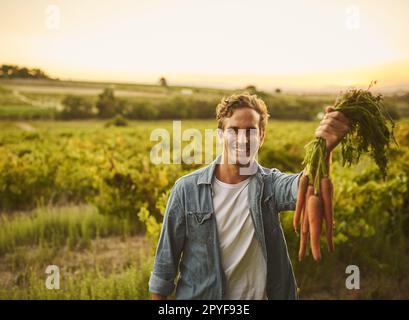 This is what time and effort looks like. young man holding a bunch of carrots and smiling with his farm in the background. Stock Photo