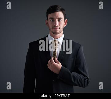 Where a necktie or a noose. Its your choice. Studio portrait of a young businessman with a noose tied around his neck for a tie against a gray background. Stock Photo