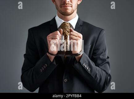 Corporate criminal. Studio shot of a handcuffed businessman with a noose tied around his neck for a tie against a gray background. Stock Photo