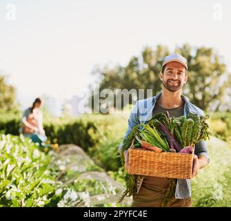 Delivering freshness to your dinner plate. Portrait of a happy young farmer harvesting herbs and vegetables in a basket on his farm. Stock Photo