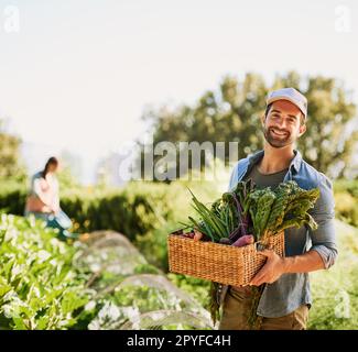 We only grow the best. Portrait of a happy young farmer harvesting herbs and vegetables in a basket on his farm. Stock Photo