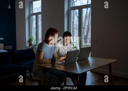 Young interracial couple looking at laptop discussing online family business, working late at home Stock Photo