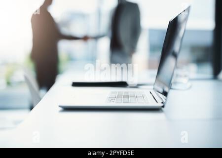 Making a success of the day. a laptop on a boardroom desk with two businessmen blurred in the background. Stock Photo