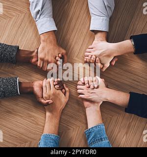 There is more power in unity than division. High angle shot of a group of unidentifiable businesspeople holding hands together in unity. Stock Photo