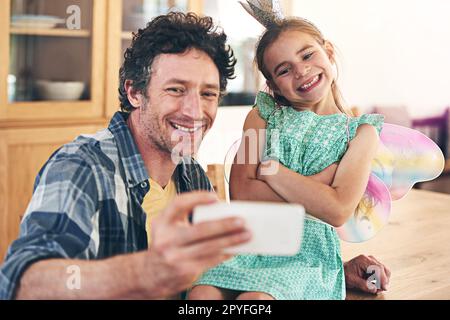 She out-selfies me every time. a happy father and daughter taking a selfie together on a mobile phone at home. Stock Photo