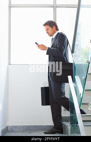 Business man using cellphone on stairs. Full length of handsome middle aged business man using cellphone on stairs. Stock Photo
