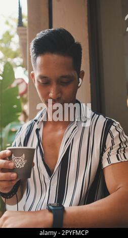 Young man sits outside and drinks coffee Stock Photo