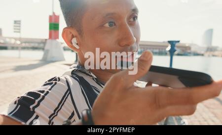 Close up, young man tourist sits on bench on the pier and sends voice message from mobile phone Stock Photo