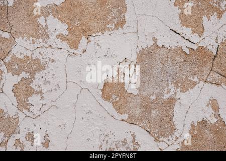 Old cracked weathered painted wall background texture. Beige dirty peeled plaster wall with falling off flakes of paint Stock Photo