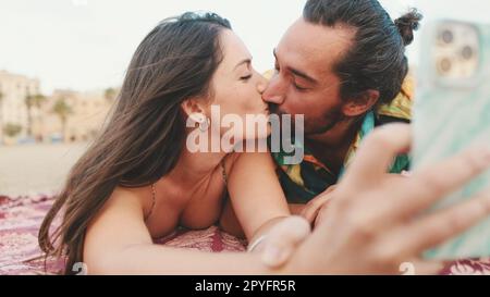 Man and woman kissing and making video call using mobile phone on the beach Stock Photo