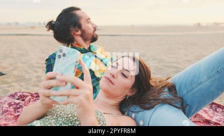 Young couple relaxing on the beach, talking, using mobile phone Stock Photo