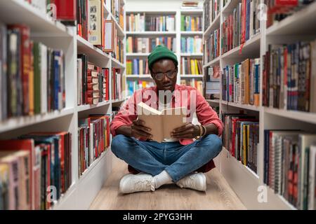 Student african american man reading research textbook in university library sitting on floor. Stock Photo