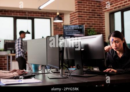 Pensive asian tech enginner working on code development and brainstorming ideas to create html script. Thoughtful software developer thinking about database server in it agency office. Stock Photo