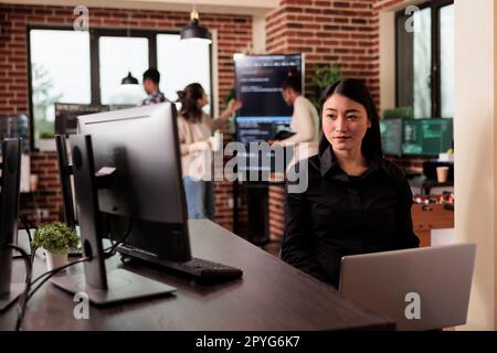 Asian programmer typing machine learning server code, sitting at desk table in it software company. Programming engineer working on database system with coding script in it developing office Stock Photo