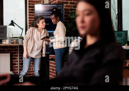 Two software developers analyzing source code looking for errors, checking big tv monitor in it agency office. Tech enginners working on cyber security innovation in it programming agency. Stock Photo