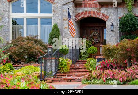 Entrance and window to beautiful rock upscale house with lush landscaping and American flag and wreath on door Stock Photo