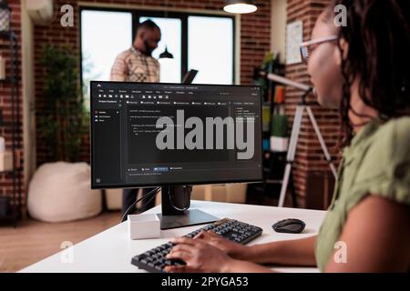 African american software developer debugging source code algorithm looking at computer screen while roommate is using laptop. Freelance coder writing software working remote from home. Stock Photo