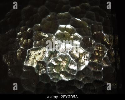 Corrugated glass, rear light source. Play of glare and reflections on a transparent uneven surface. Dark and light abstract asymmetric multi-illuminated planes. Abstract bumpy golden background. Stock Photo