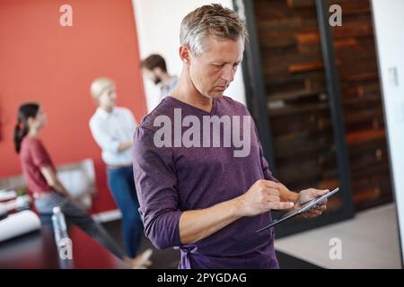 Hes getting used to the new tablet. a handsome designer using a tablet with his coworkers in the background. Stock Photo