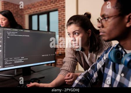 Tech enginner asking app designer for help with html code, pointing at database script on terminal window. Team of programming engineers working on app developing program in it agency. Stock Photo