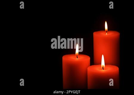 Three red wax candles burning in darkness on dark background Stock Photo