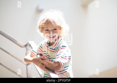 Little boy on stairs. Sunny staircase in new family home. Child climbing up stairs. Home interior. White stairway. Kids safety. Stock Photo