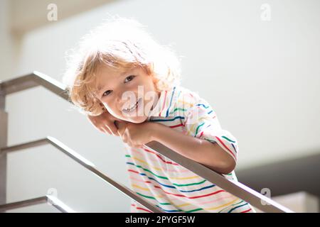 Little boy on stairs. Sunny staircase in new family home. Child climbing up stairs. Home interior. White stairway. Kids safety. Stock Photo