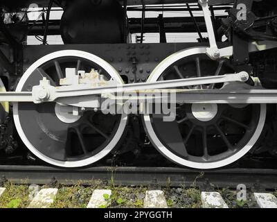 Retro train two wheels. Sleepers and rails, mechanisms, pistons and guides. Locomotive of the 19th early 20th century with a steam engine. Black and white wheels with green grass. Vintage style Stock Photo