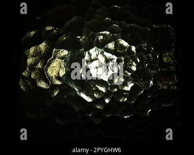 Corrugated glass, rear light source. Play of glare and reflections on a transparent uneven surface. Dark and light abstract asymmetric multi-illuminated planes. Abstract bumpy background Stock Photo