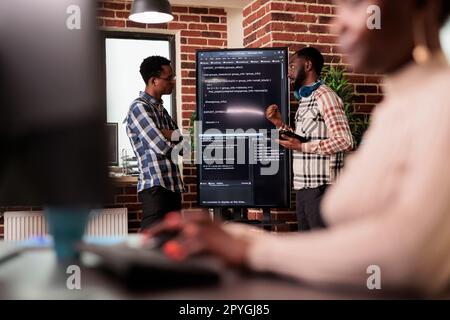 Programming engineers analyzing html code standing in front of big screen, checking errors in artificial intelligence project. Software developers working on machine learning software in it agency Stock Photo