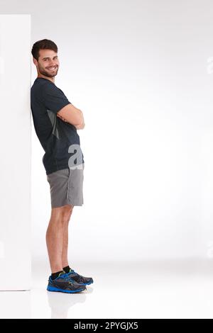 Ive got nothing to worry about. Studio shot of a smiling young man leaning casually against a blank billboard. Stock Photo