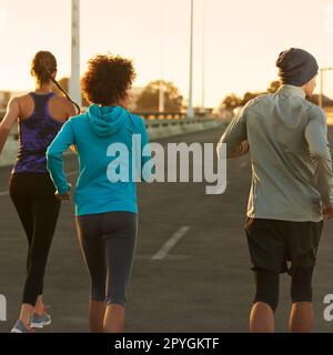 Not a car to bother us. Rearview shot of three young joggers running down an empty street at dawn. Stock Photo