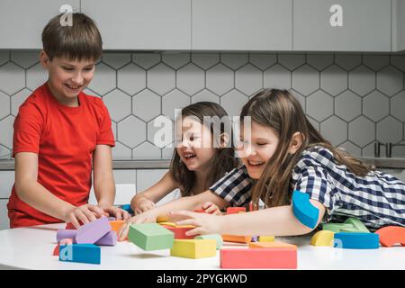 Laughing, funny and playful children of girls fooling around and boy playing with colorful bricks and building elements Stock Photo