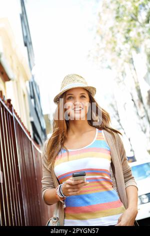 With this app Ill never get lost. A gorgeous young woman wearing casual summer clothes walking down a city street while texting on her cellphone. Stock Photo