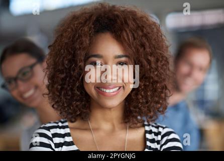 Straight forward confidence. Closeup portrait of a confident young woman with friendly coworkers peeping out behind her. Stock Photo