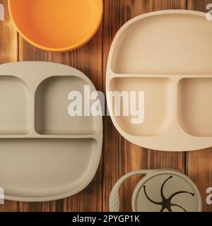 Modern colorful pastel silicone food trays, bowl and snack cup on brown wooden table. Baby tableware, first feeding. Stock Photo
