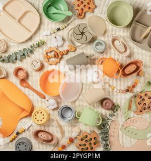 Pastel silicone collection of tableware, cutlery, bibs, accessories, wooden toys for children on white cloth background. Stock Photo
