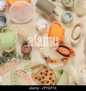 Pastel silicone collection of tableware, cutlery, bibs, accessories and wooden toys for children on cloth background. Stock Photo