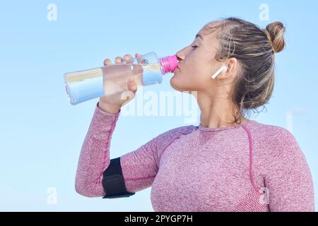 Woman runner, water bottle and music with earphones for focus, workout and outdoor training for health. Girl, wellness and hydration for running, exercise or streaming audio in summer for strong body Stock Photo
