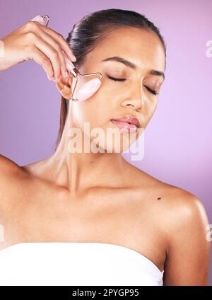 Skincare, facial roller and woman in studio on purple background for wellness, beauty products and massage. Dermatology, spa aesthetic and girl with treatment for face, cosmetics and healthy skin Stock Photo