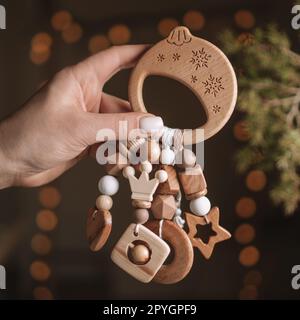 Wooden Christmas ball shaped childrens teether with silicone beads in woman hand, dark background with garland lights Stock Photo