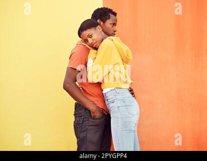 Love, hug and comfort with a black couple together outside on a color wall background for romance or dating. Hugging, date and consoling with a man and woman holding each other in support or care Stock Photo