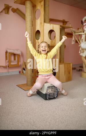 Cheerful girl sitting on cage with cat over animal shelter Stock Photo