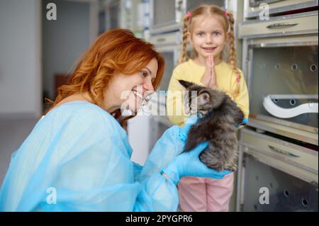 Mother holding little kitten and her daughter folding hand in pray position Stock Photo